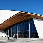 An exterior architectural shot of the A. Le Coq Arena in Tallinn, Estonia, showcasing its modern design and integration into the urban landscape. The stadium features clean lines and a contemporary aesthetic under a clear sky. A few individuals are walking near the stadium entrance, dressed in fully clothed, modest business casual attire. The scene is well-lit, professional photography, high quality, safe for work, appropriate content, family-friendly. Perfect anatomy, correct proportions, natural pose, well-formed hands, proper finger count, natural body proportions.